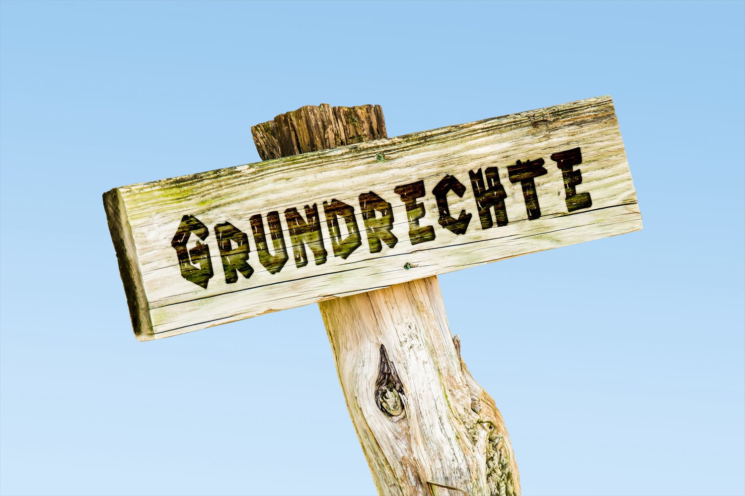 Verwittertes Holzschild „Grundrechte“ vor blauem Himmel
