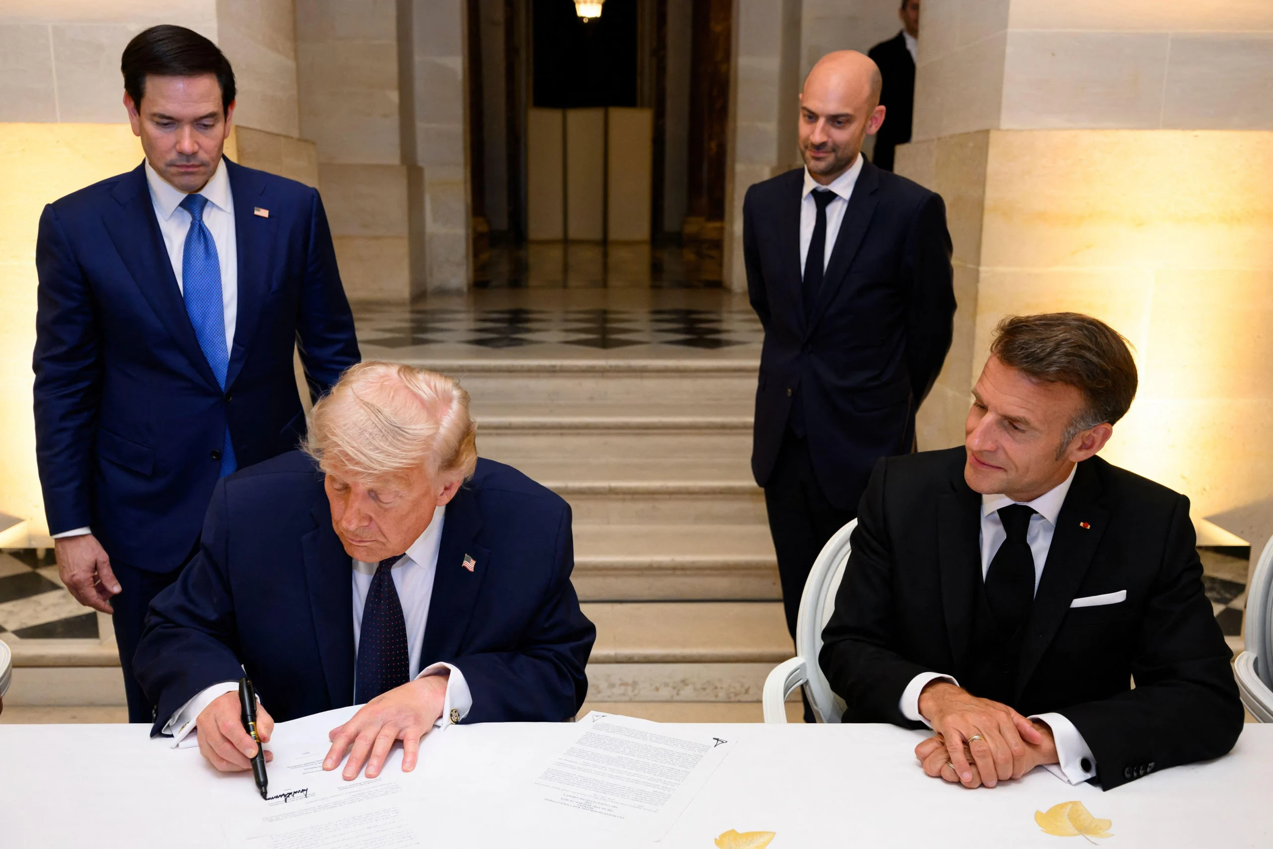 Foto: Donald Trump unterzeichnet im Schloss Versailles die Absichtserklärung mit dem Iran, neben ihm Emmanuel Macron, hinter ihm Marco Rubio, 17. Juni 2026