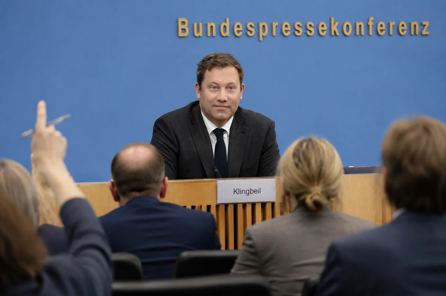 KI-generierte Illustration: Lars Klingbeil auf dem Podium der Bundespressekonferenz, Journalisten melden sich zu Wort
