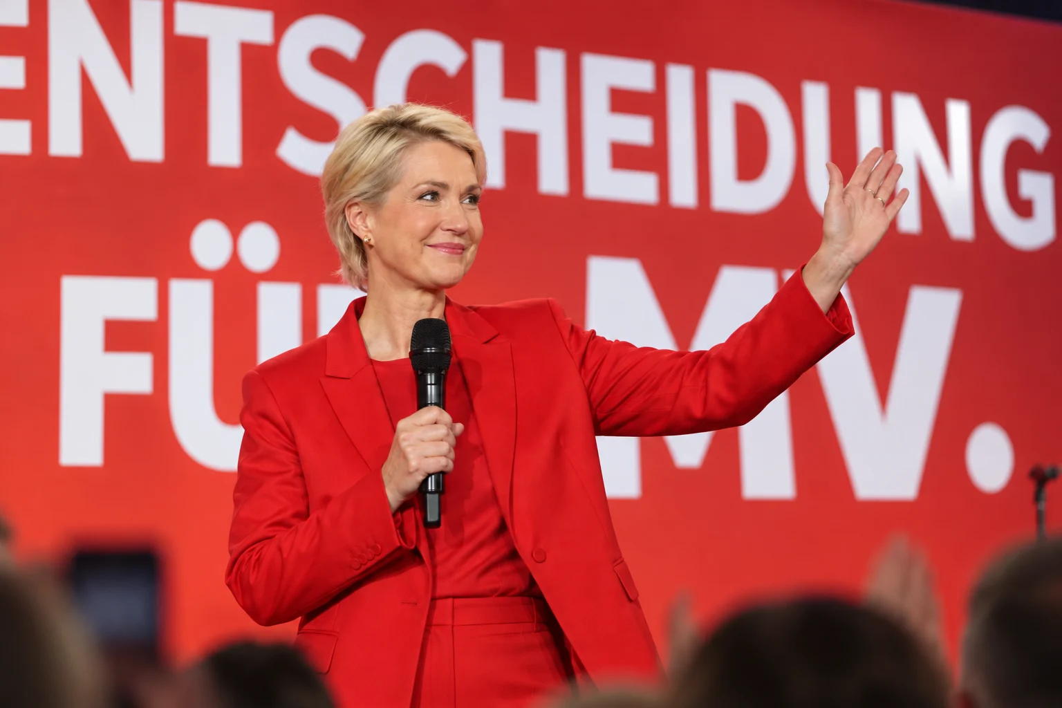KI-generierte Illustration: Manuela Schwesig im roten Anzug winkt auf der SPD-Wahlparty vor dem Schriftzug „Entscheidung für MV“